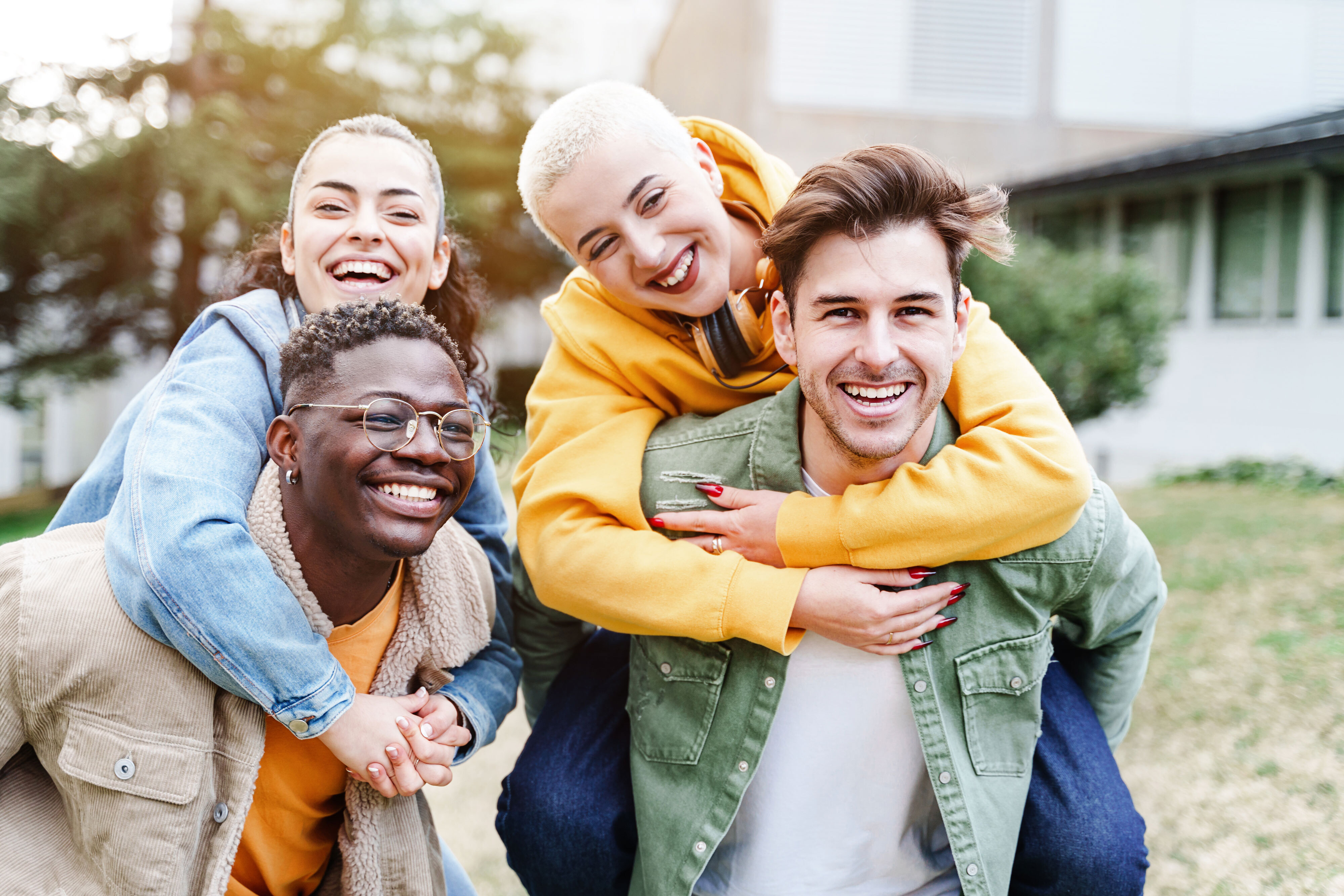 Four laughing college students, two piggyback on the others.