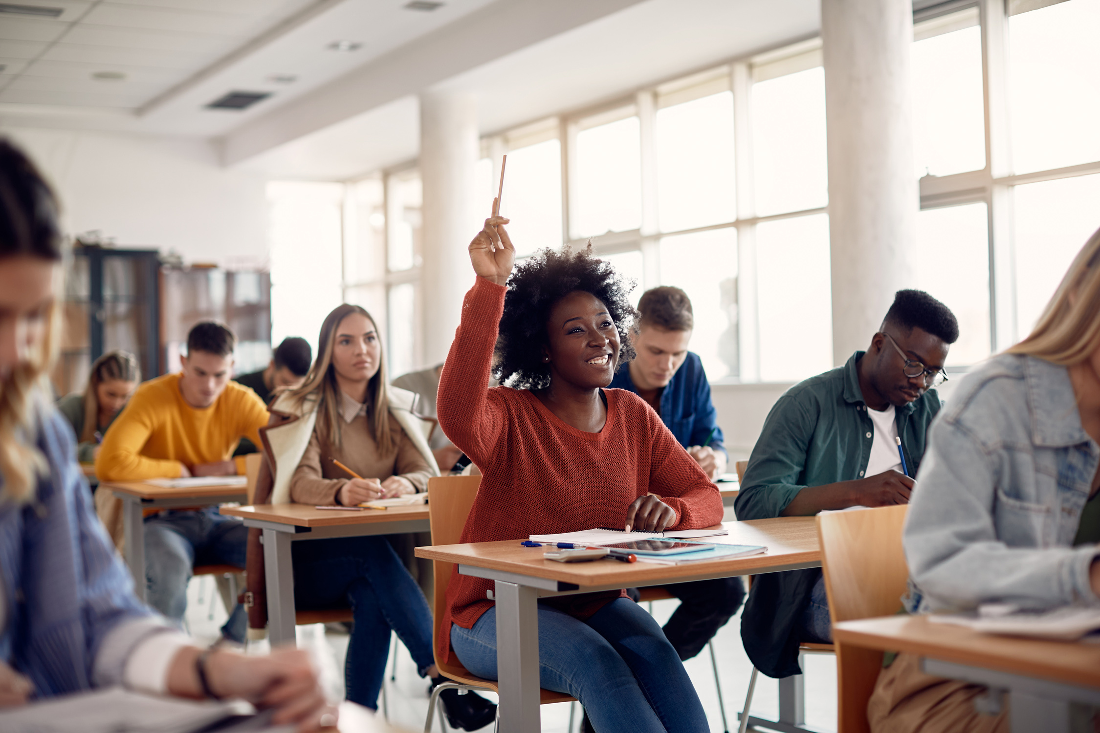 student in college classroom raises hand