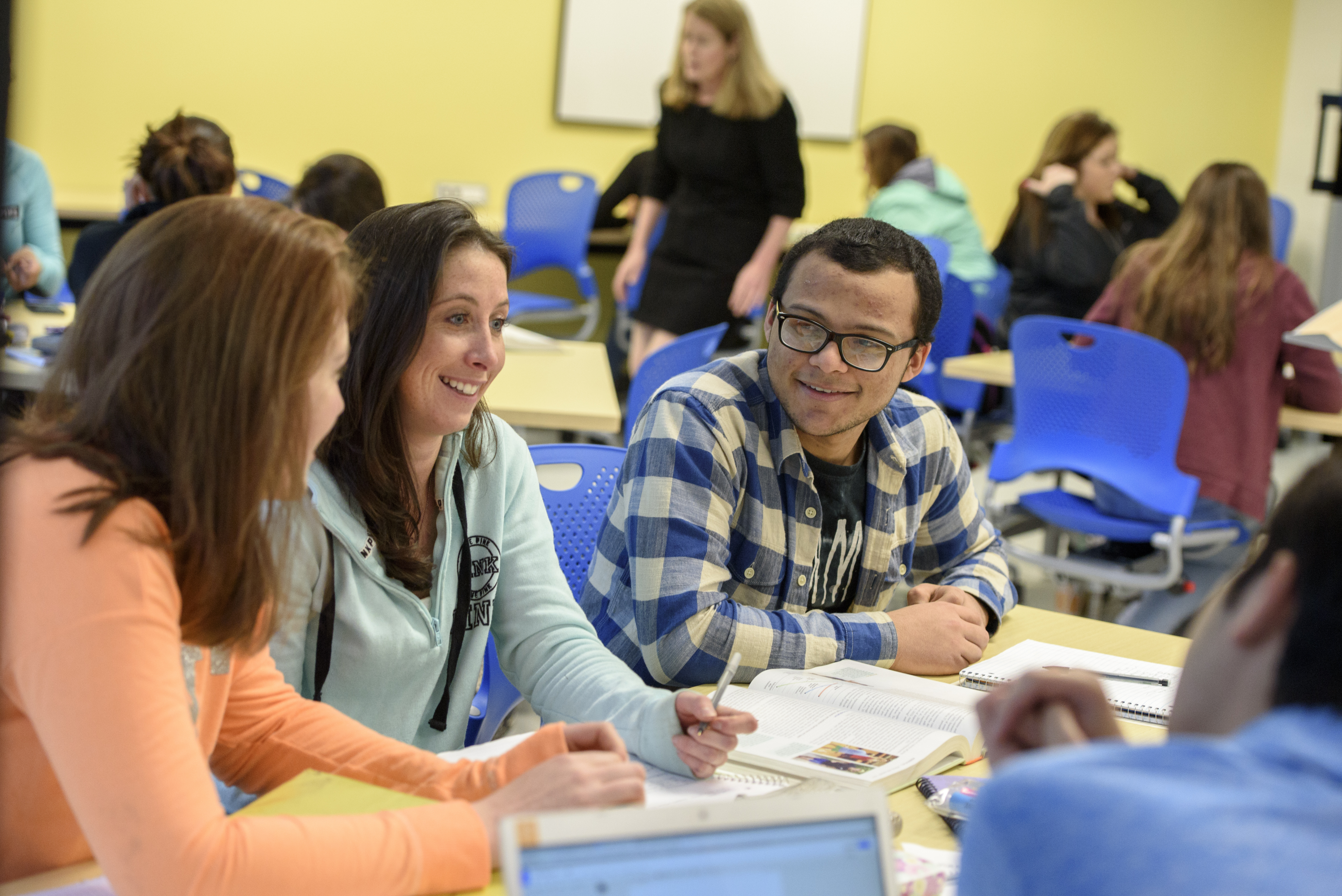 Students sit at table together with books talking